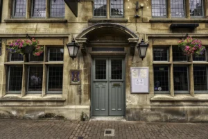 Two hanging baskets outside a grand building with large doorway and leaded light windows