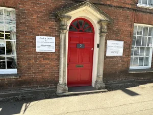 A red brick property with a red door and windows either side