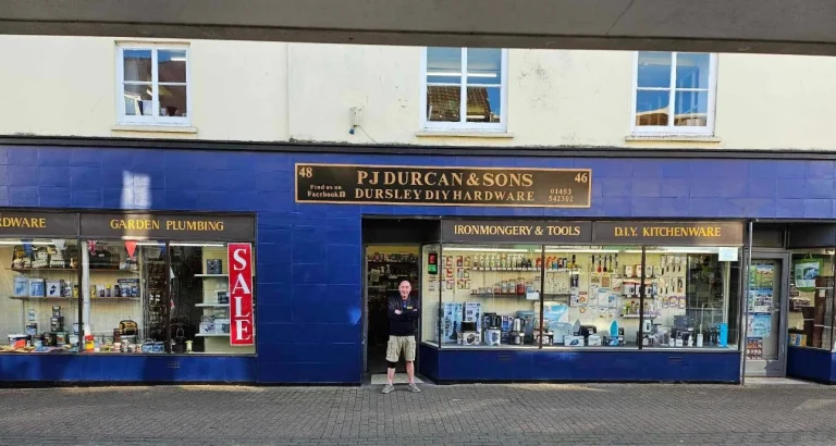 Front of blue painted shop on the high street called Durcan and Sons with the owner standing outside the door.
