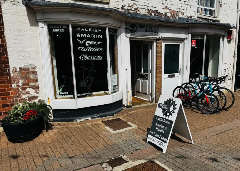 Front of a bay windowed shop on the high street called Dursley Meccanica with bicycles and a-frame advertisement board outside.